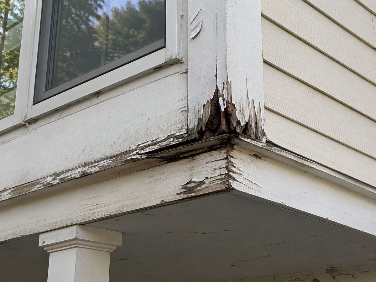 Wood trim before carpentry repair — rotted wood, peeling paint, and exposed damage at corner soffit